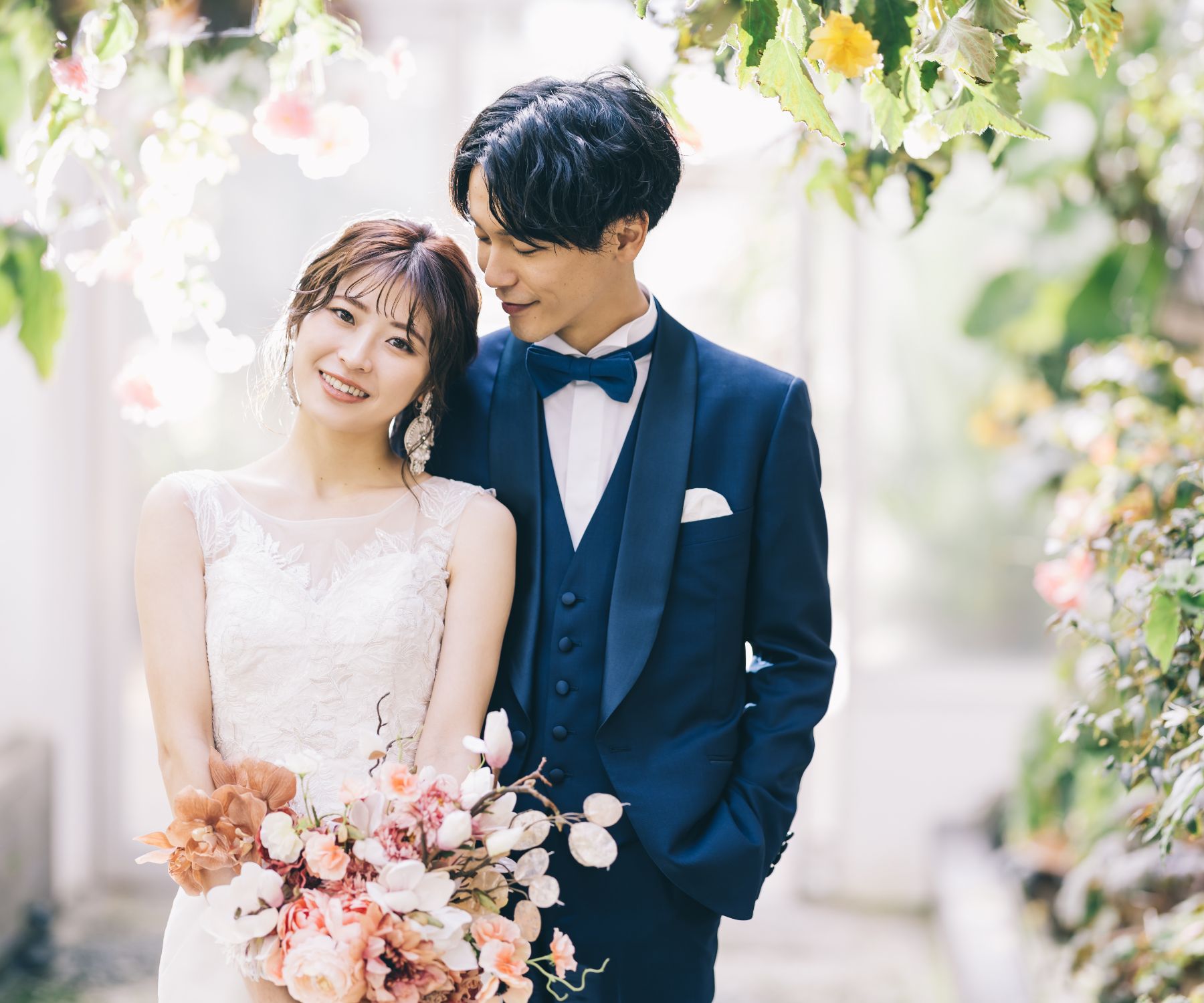 草花のトンネルの下で微笑む新郎新婦様のウェディングフォト