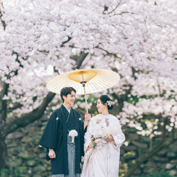 白い和傘のしたで微笑みあう新郎様の和装前撮り