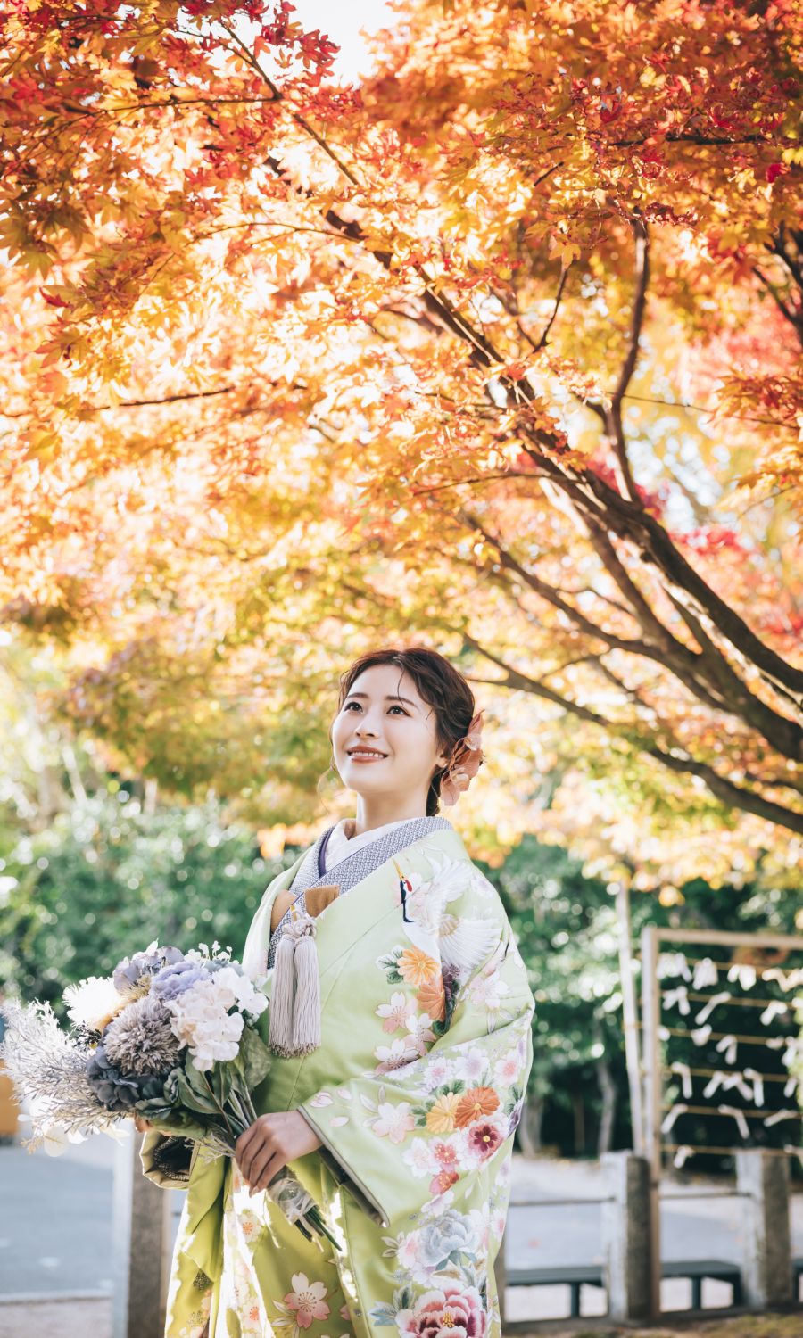満開の紅葉の下、花束をもって笑う新婦様のソロショット