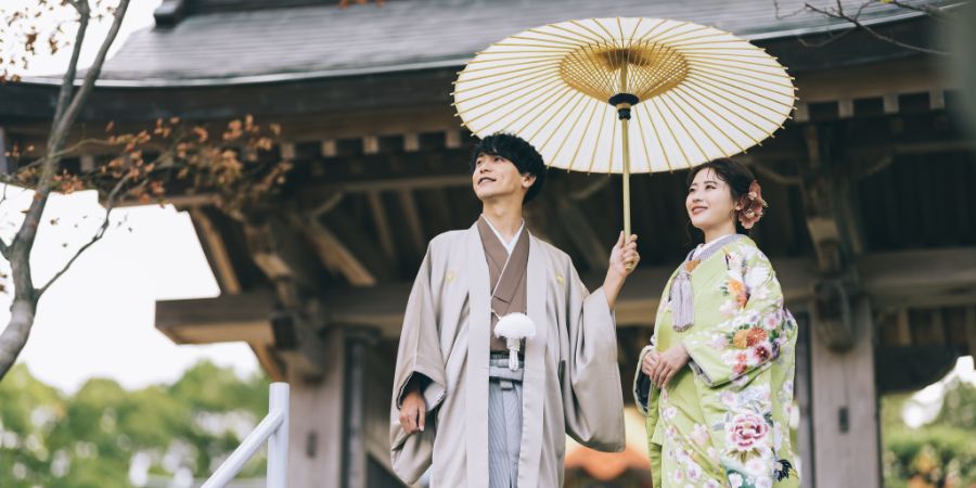門の下で白い和傘をさして佇む新郎新婦様の和装前撮り
