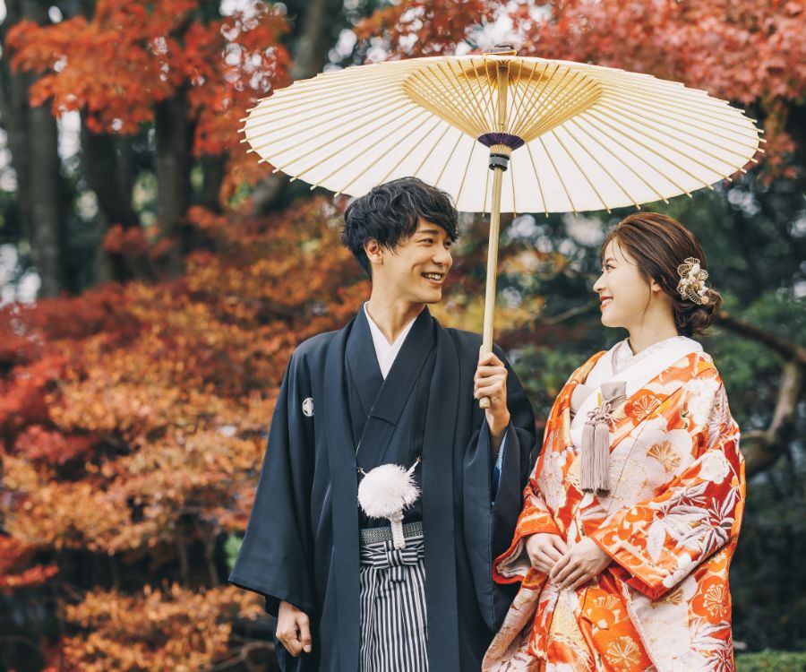 紅葉を背に白い和傘の下で微笑む新郎新婦様の結婚写真