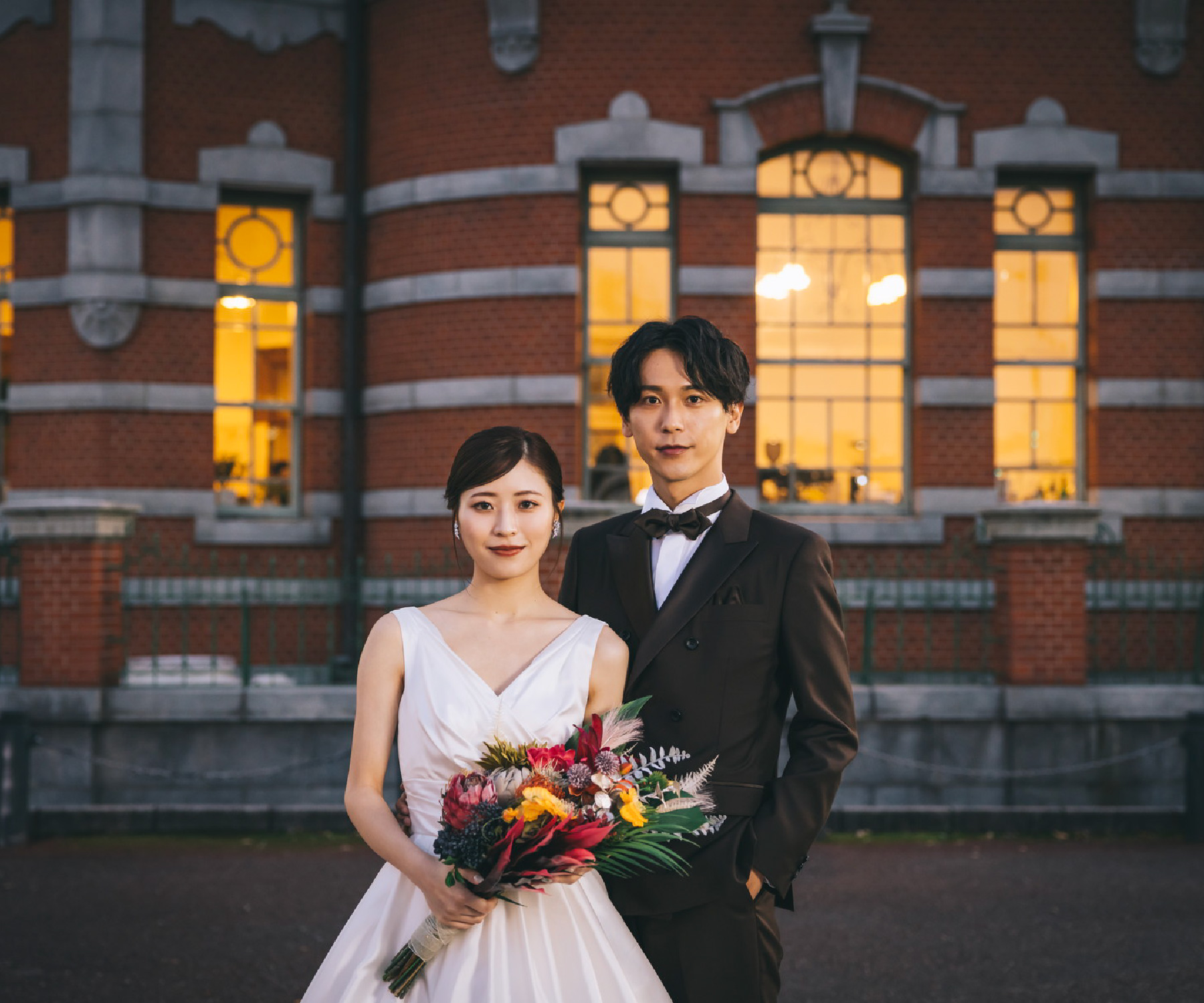 夕方の赤煉瓦文化館をバックに撮る花束を持った新婦様と新郎様の結婚写真