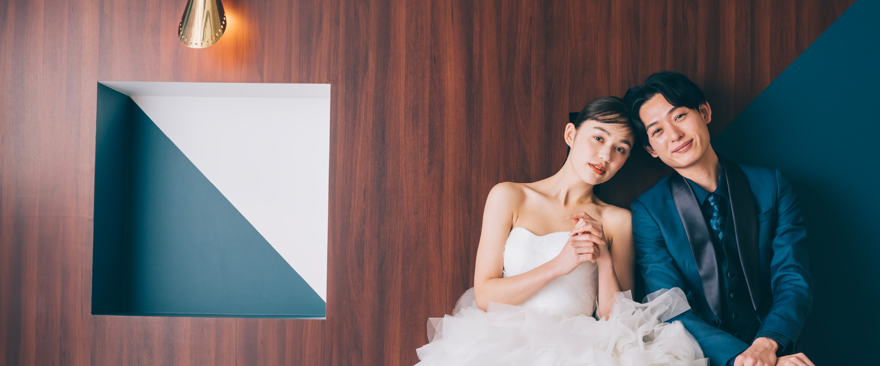 背景の青と白のコントラストに合わせたウェディングドレスと青のタキシードを着装した新郎新婦