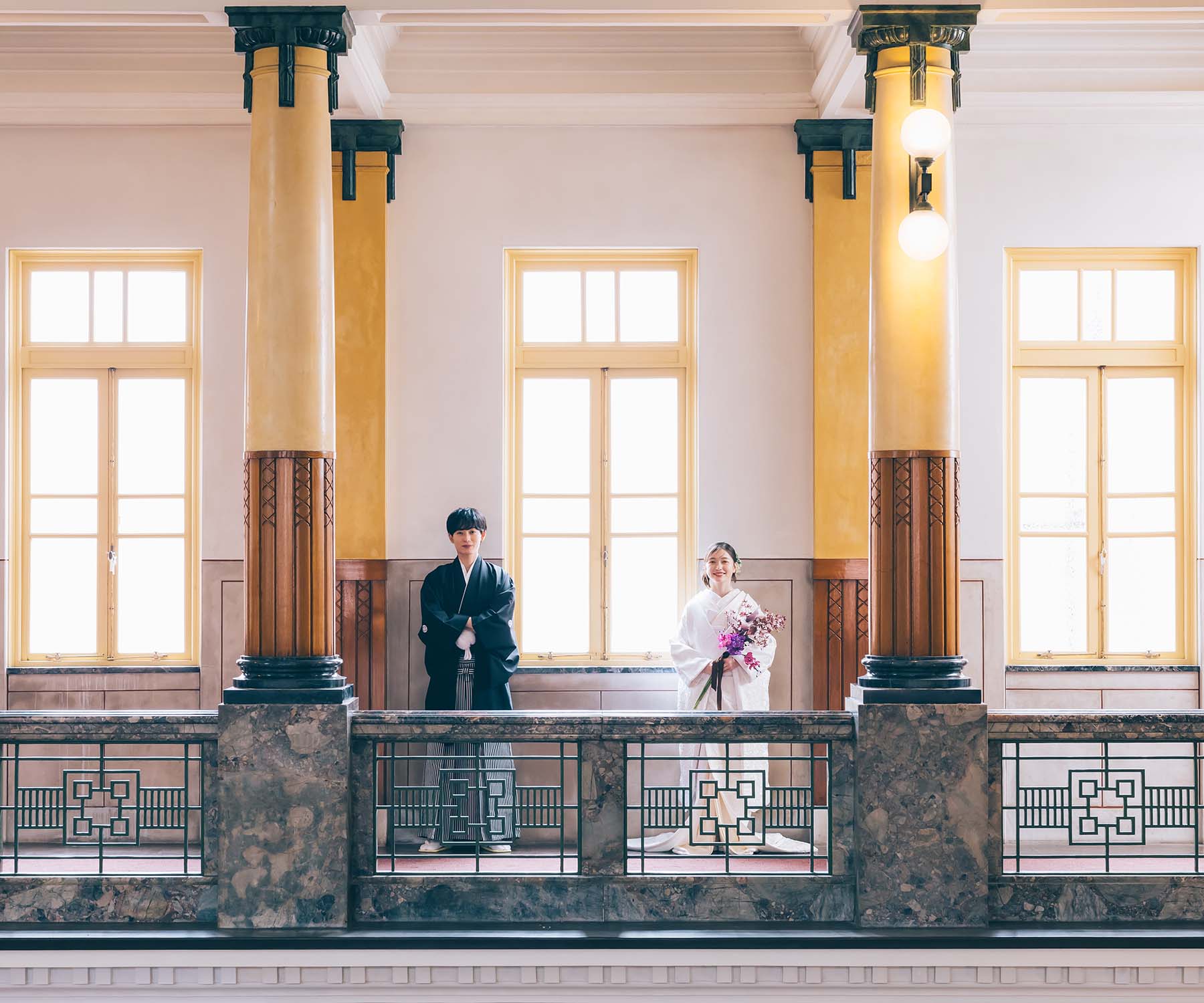 光で満ちた窓を挟んで微笑む新郎新婦様の結婚写真