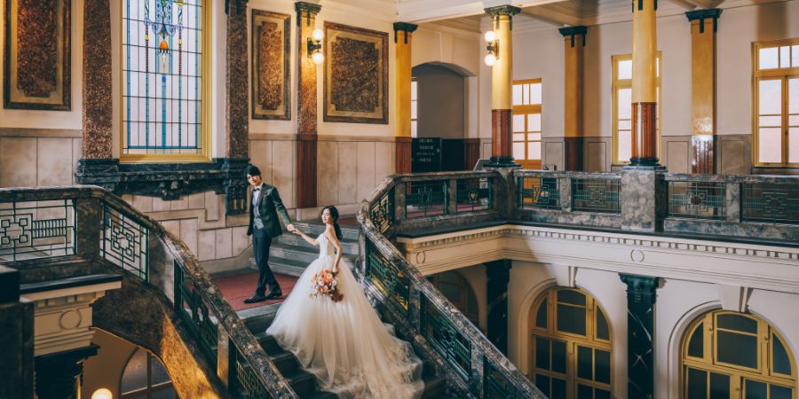 クラシカルな市政資料館の階段で新婦様をエスコートする新郎様の結婚写真