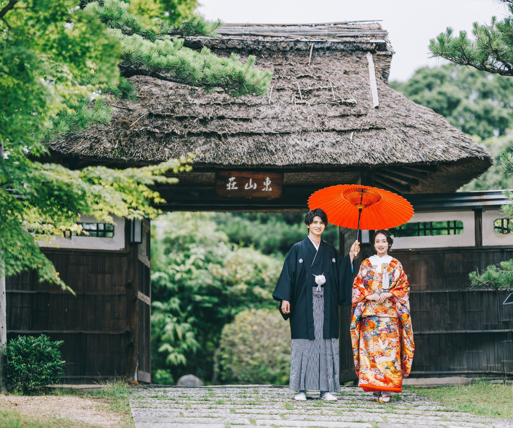 茅葺き屋根の下で和傘をさす新郎新婦様