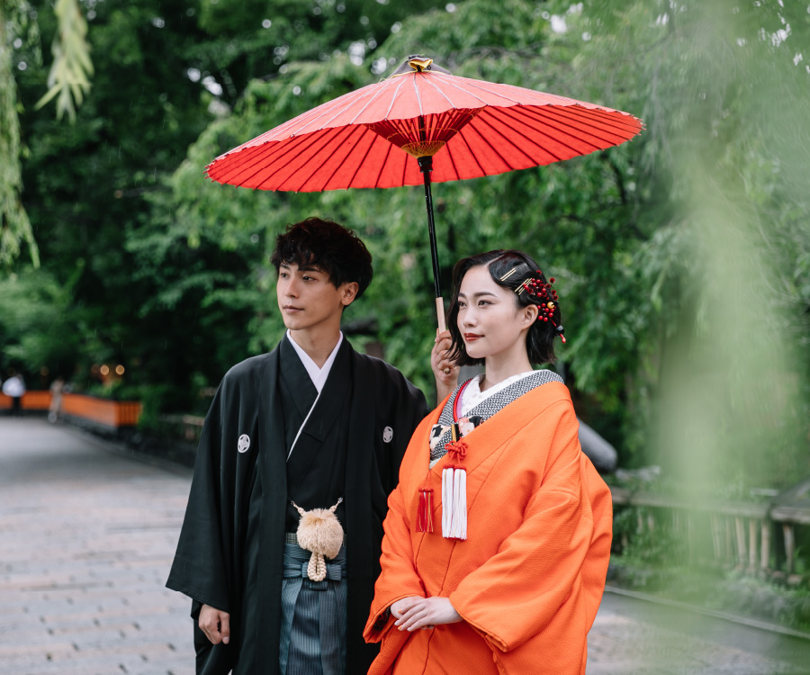 柳の下で赤い和傘で相合傘をする新郎新婦様の和装前撮り