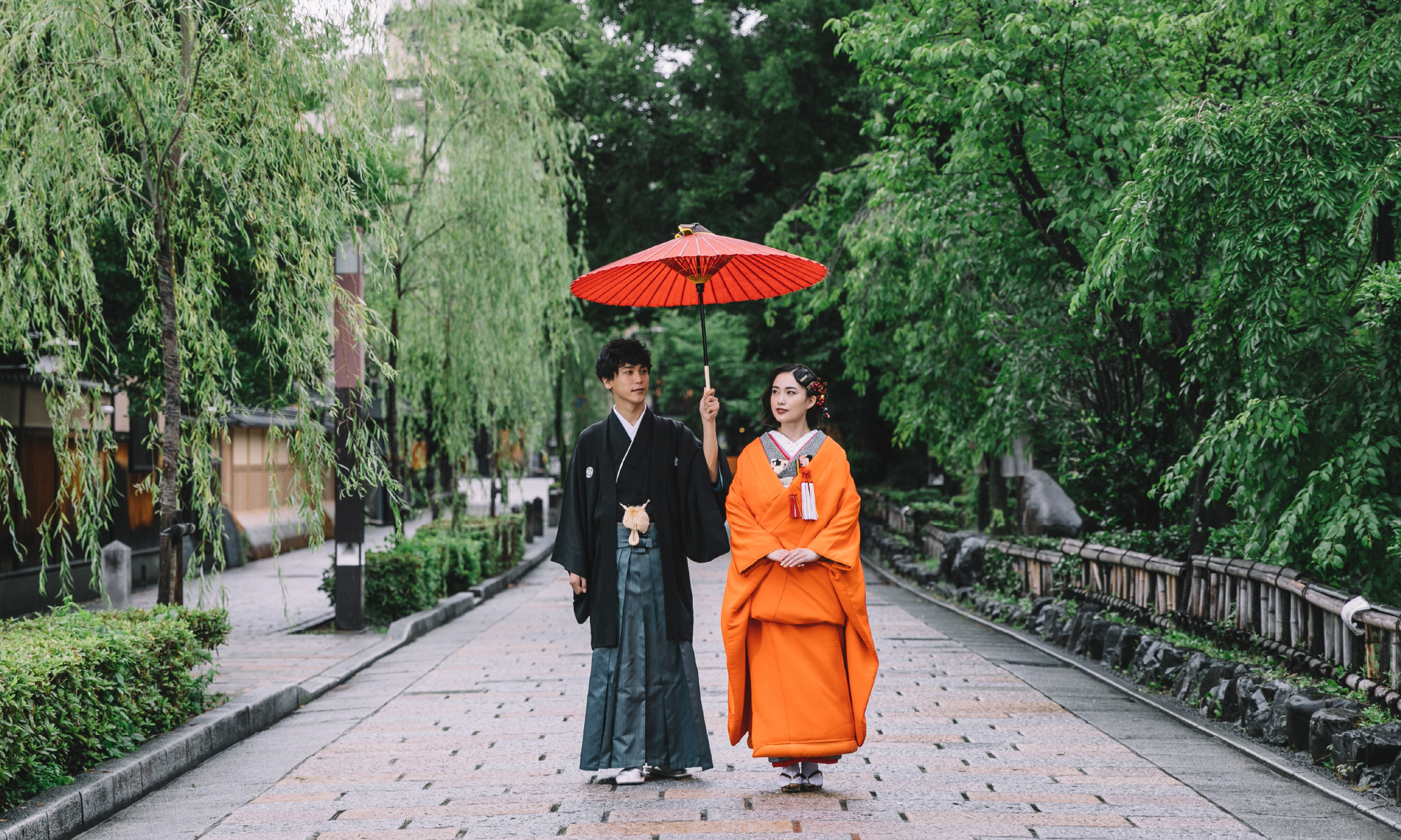 和傘を差しながら石畳の上を並んで歩く新郎新婦様の和装前撮り