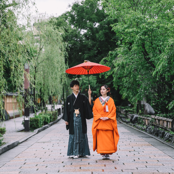 石畳の上を和傘の下並んで歩く新郎新婦様の和装前撮り