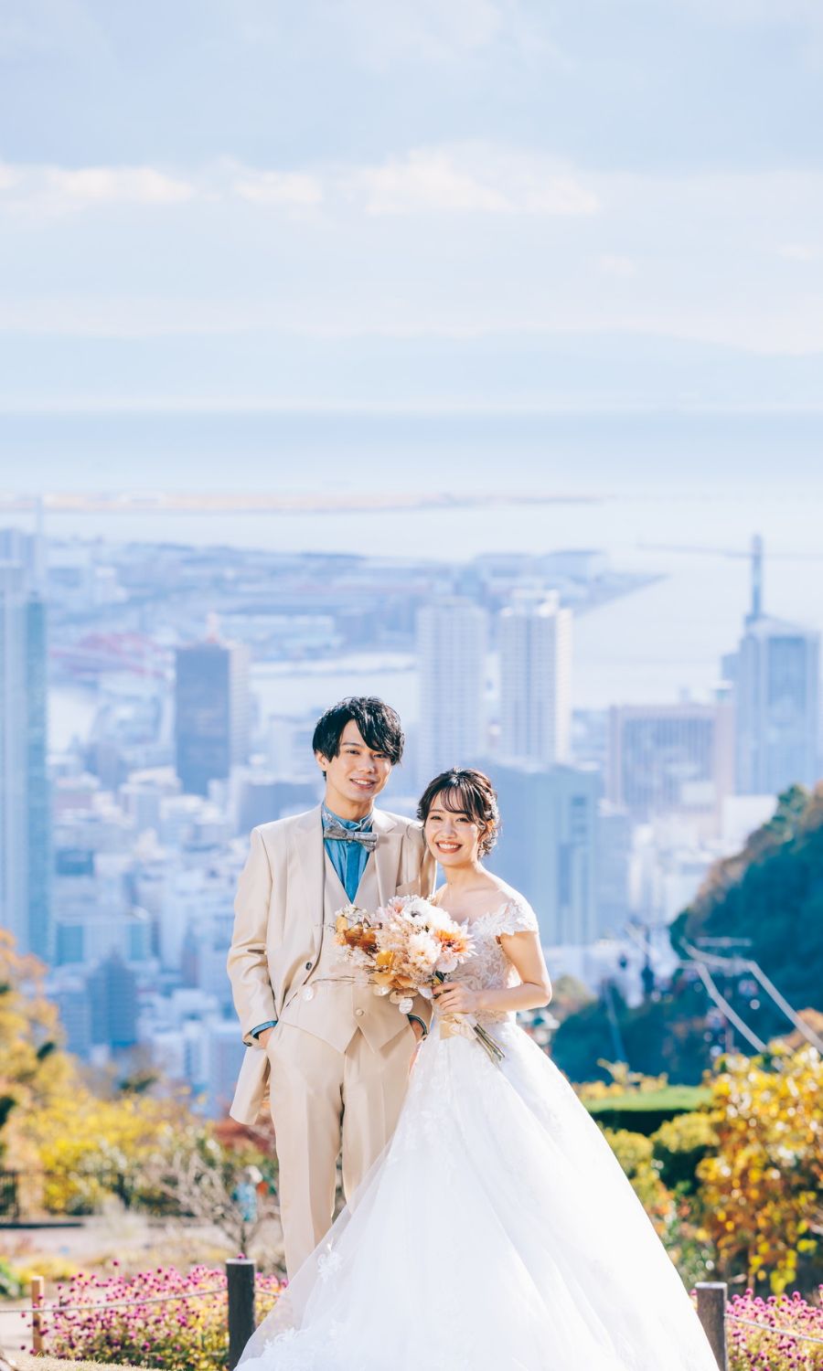 澄み切った青空の下で満面の笑みを浮かべる新郎新婦様の結婚写真