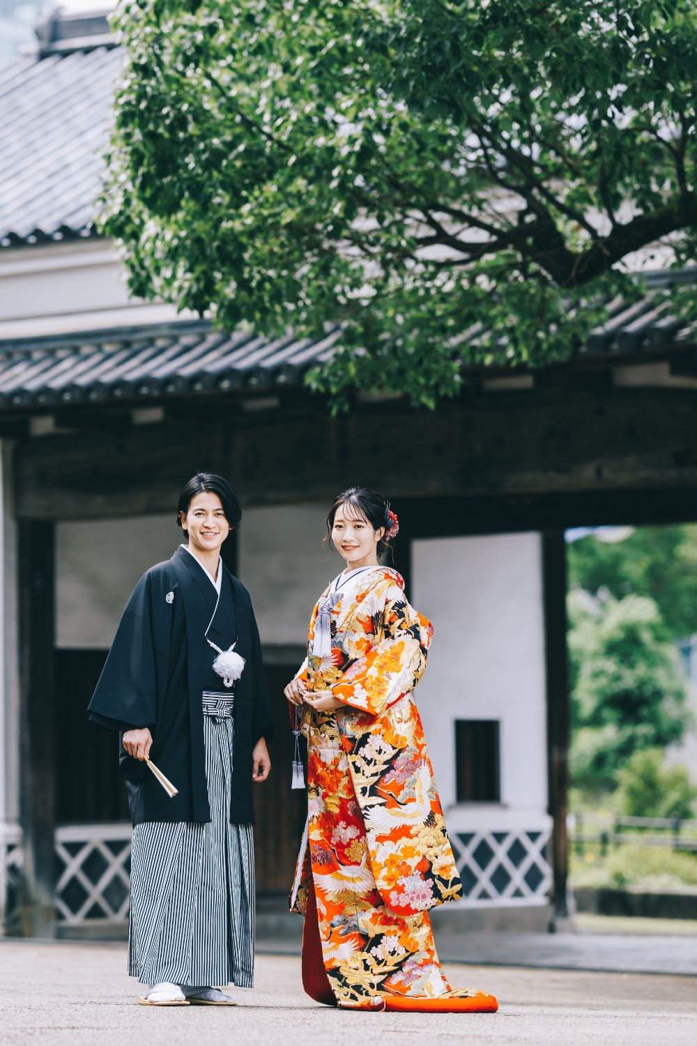 慶沢園の門をバックに微笑む新郎新婦様の和装全身ショット