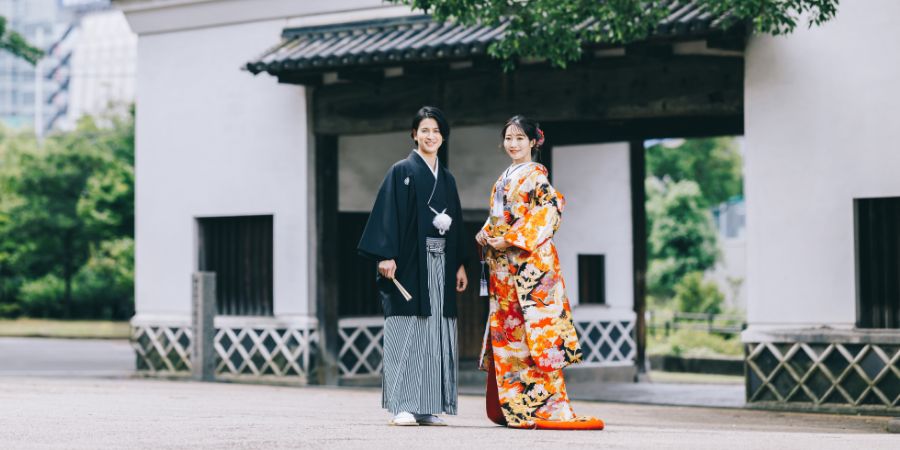 慶沢園の門をバックに微笑む新郎新婦様の和装全身ショット