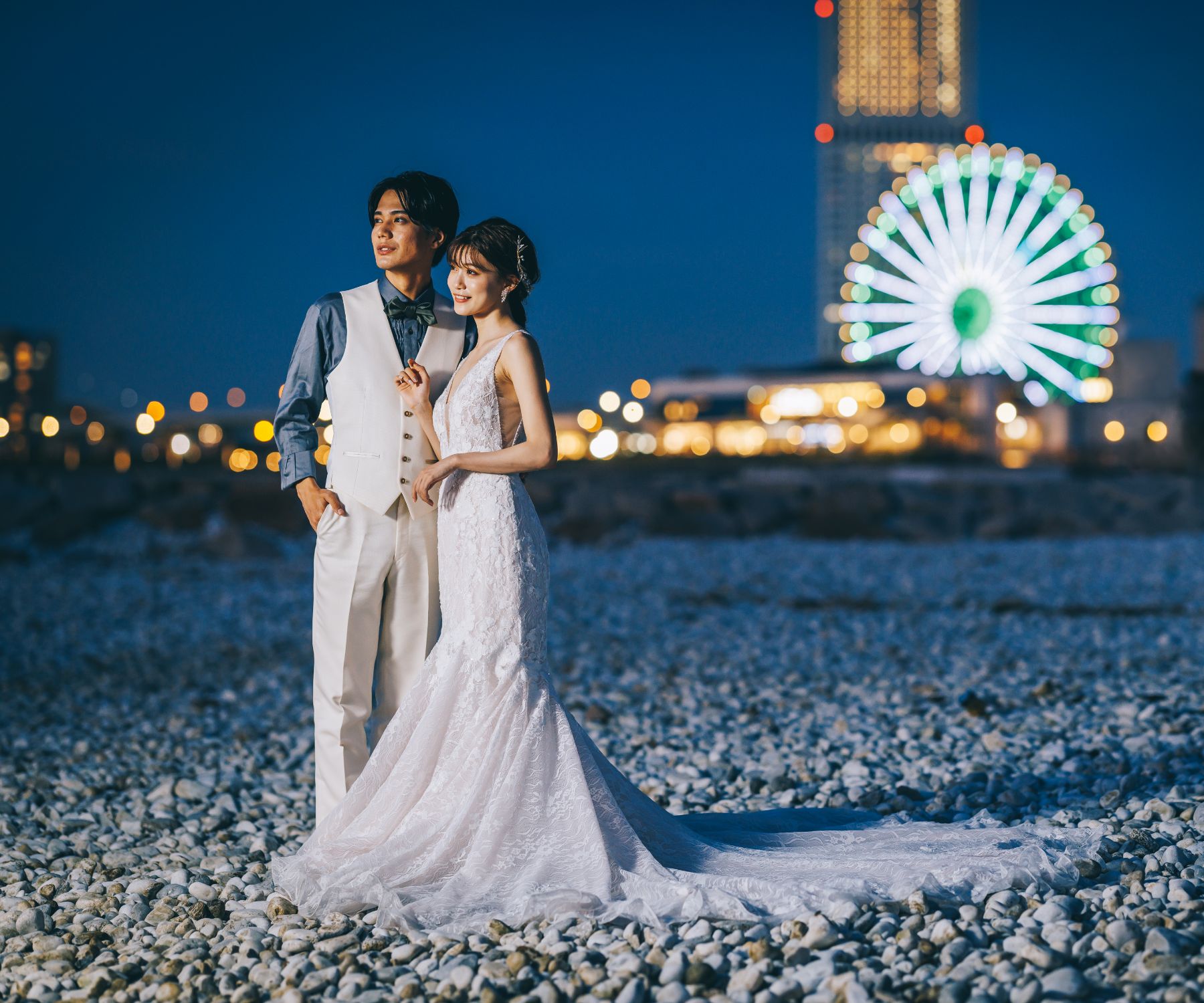 煌びやかに光る観覧車をバックに遠くを眺める新郎新婦様のナイトロケーションフォト