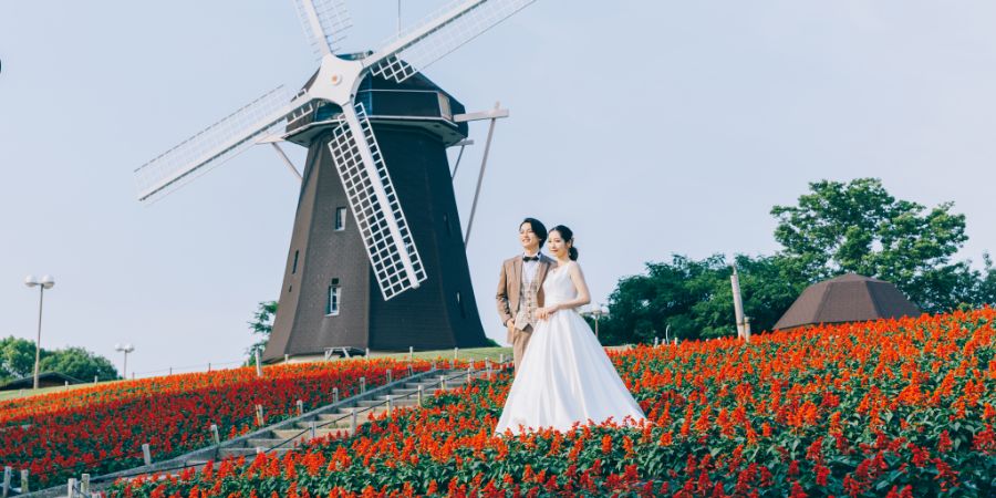 花畑に囲まれながら、レトロな風車をバックに遠くを眺める新郎新婦様のロケーションフォト