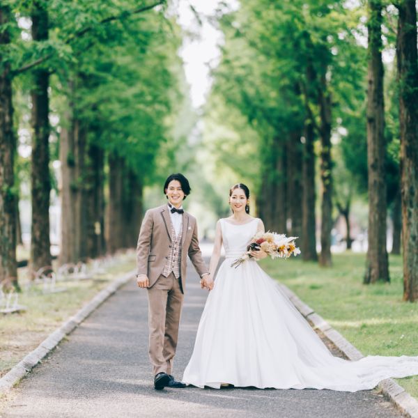 新緑で溢れた並木道で手を繋ぐ新郎新婦様のウェディングフォト