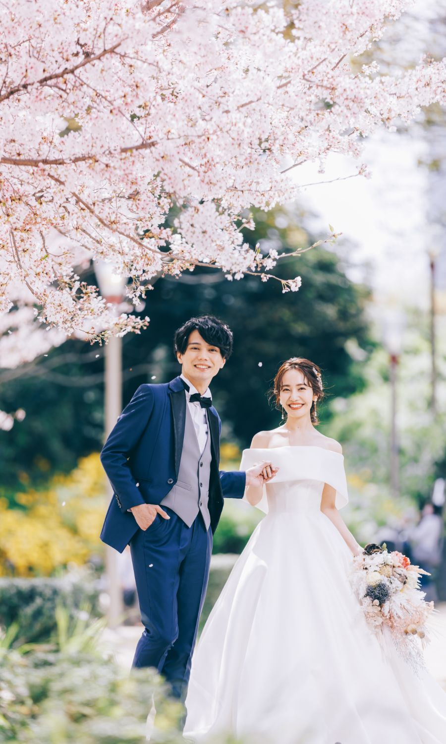 桜の木の下、満面の笑みでポーズをとる新郎新婦様の結婚写真