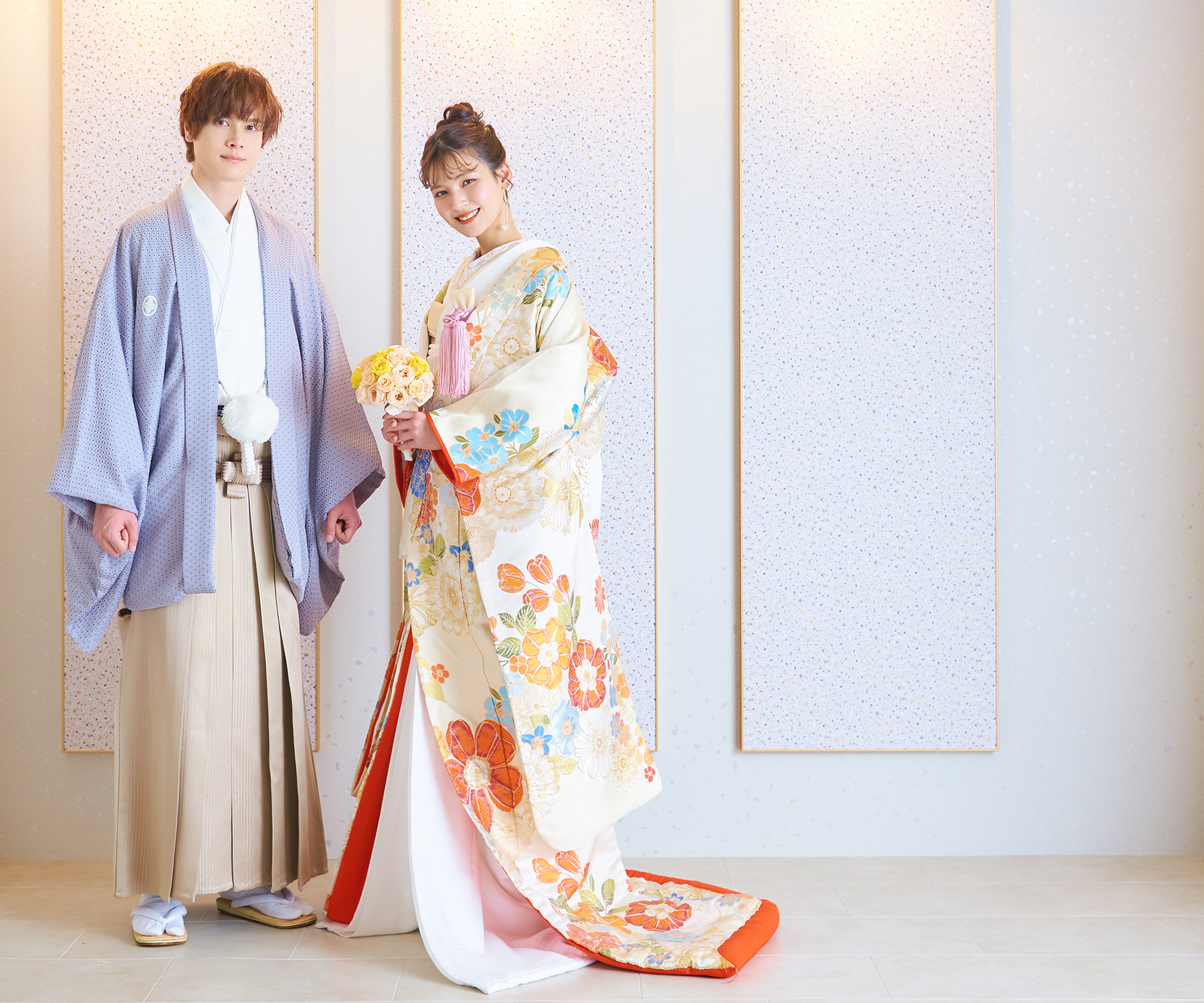           柔らかい白と淡いピンクの背景セットに調和する色打掛・袴を着た新郎新婦様の和装前撮り          