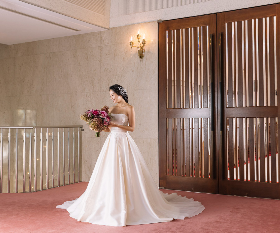 扉を背景に花束を見つめる新婦様のウェディングフォト