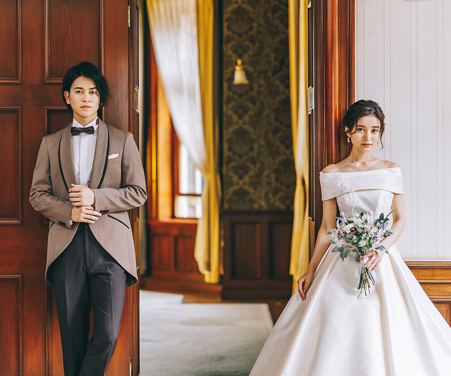 凛々しい表情で扉に寄り掛かる新郎新婦様のウェディングフォト