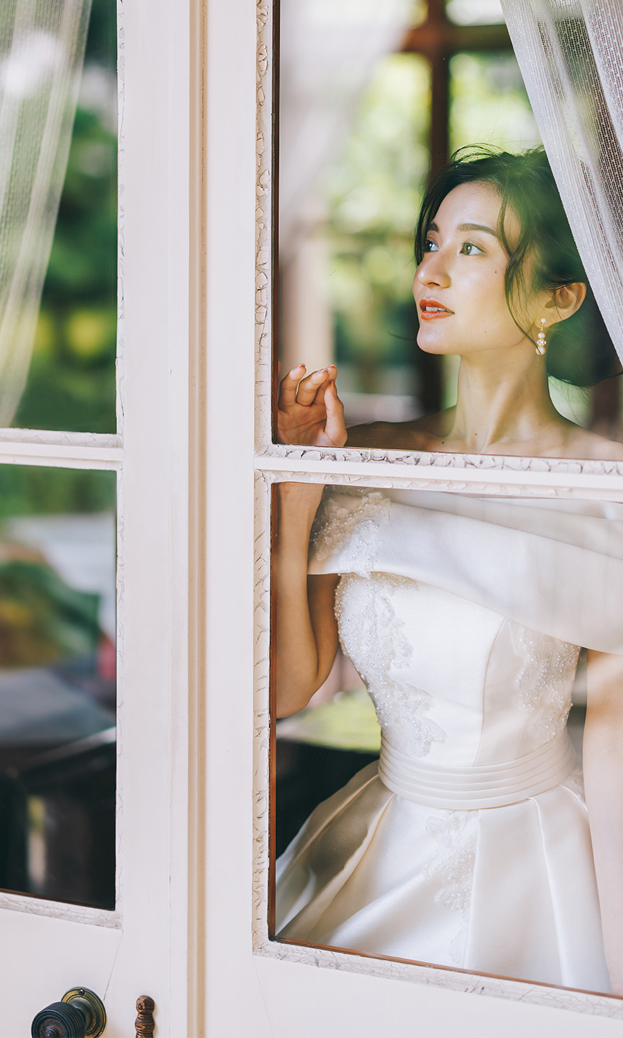 窓に顔を近づけて木々を眺める新婦様のウェディングフォト