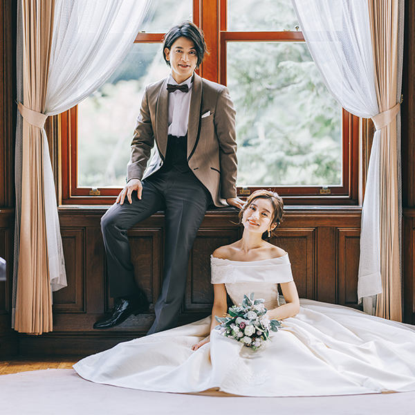 結ばれたカーテンの間で窓を背景にした新郎新婦様のウェディングフォト