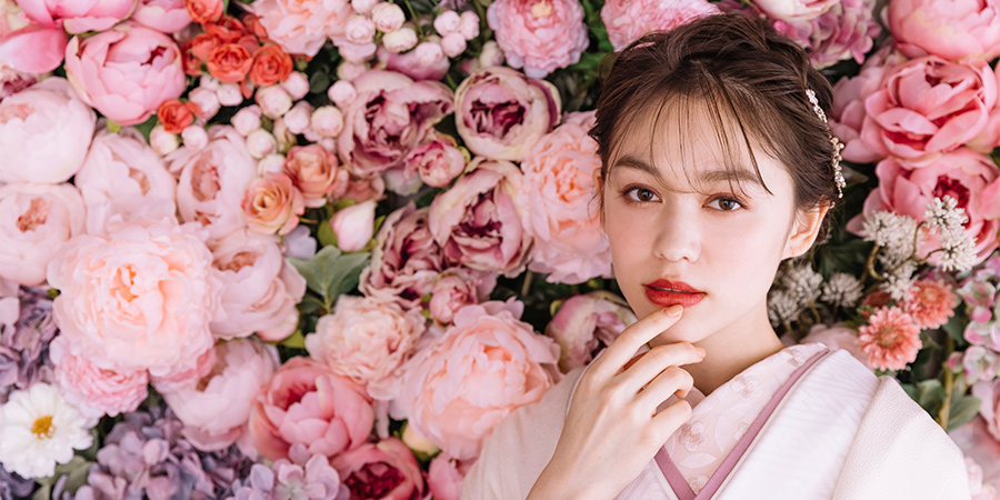 濃淡のあるピンク色のバラをバックに顎に触れる新婦様                    