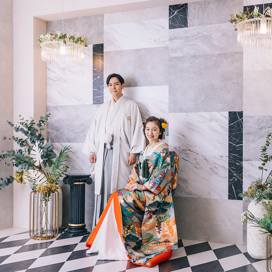 笑顔で椅子に座る新婦様の隣で微笑む新郎様の和装全身ショット                    