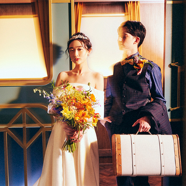      ブーケを持った新婦様とトラベルバッグを持った新郎様のロマンティックなウェディングフォト               