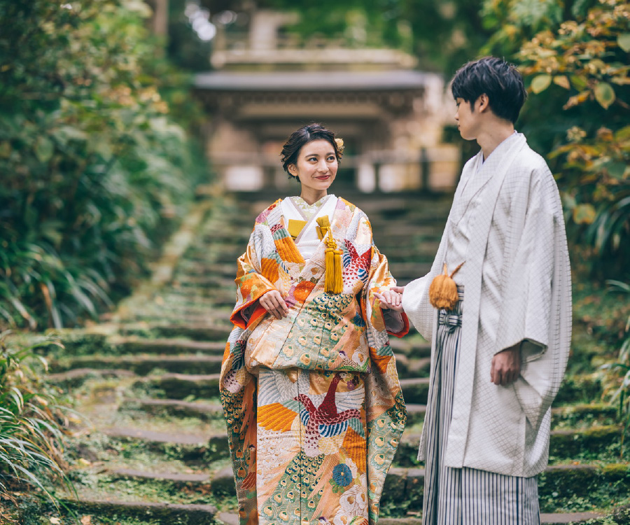 緑と紅葉が調和した木の下で葉っぱに触れる新婦様のソロショット