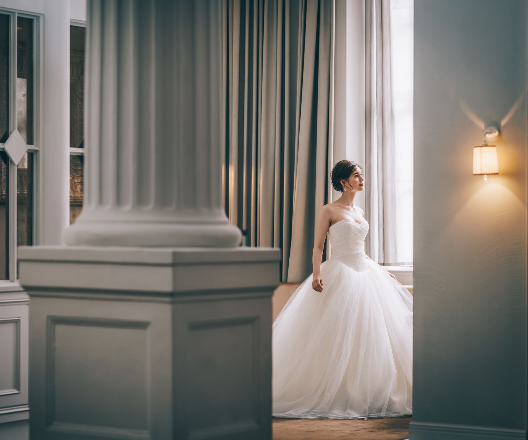柱の奥で窓の景色を眺める新婦様のソロショット