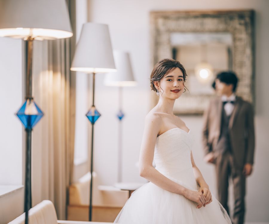 笑顔で振り返る新婦様と奥に佇む新郎様のウェディングフォト