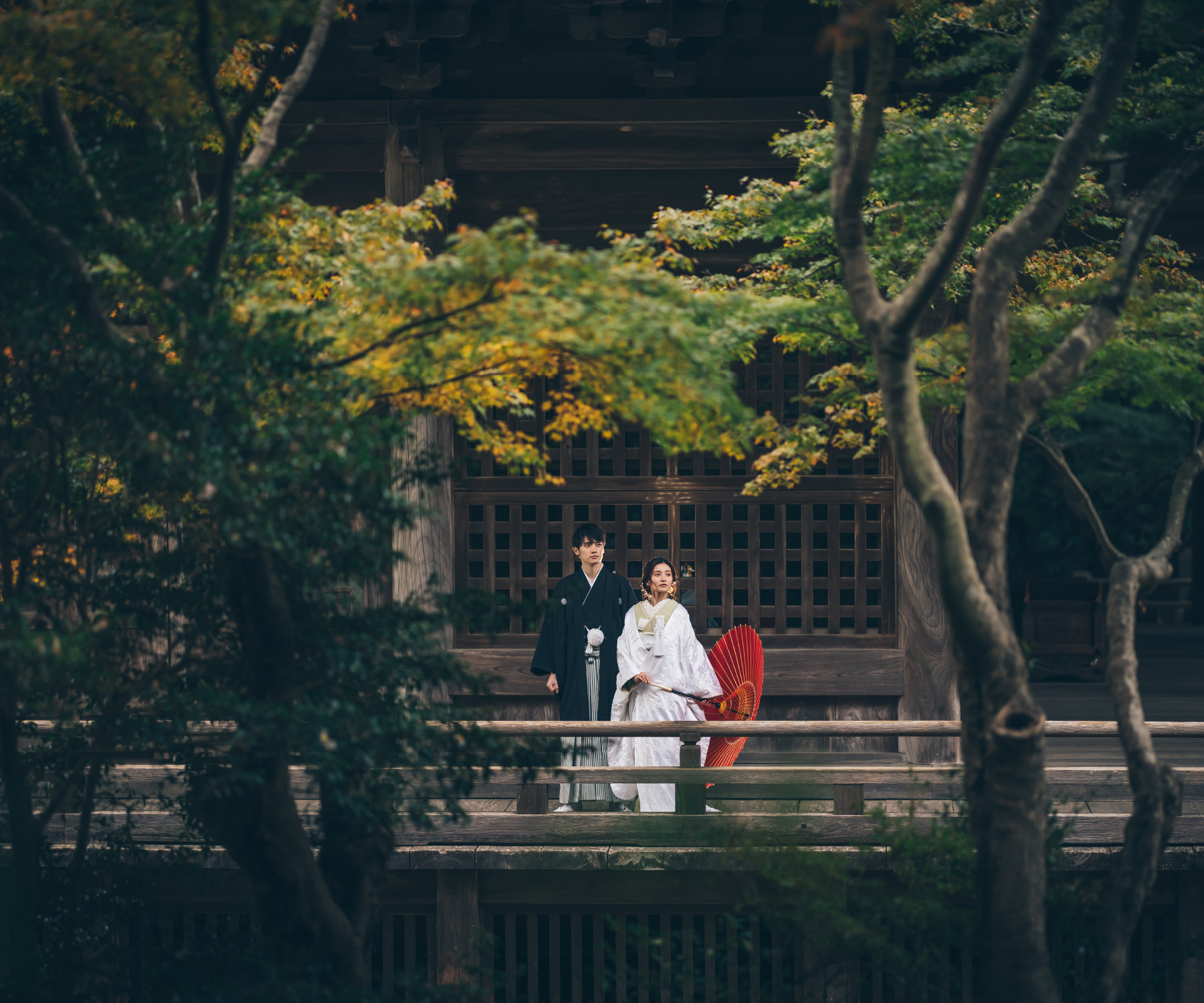 赤い和傘を持った新婦様と堂々とした佇まいの新郎様のロケーションフォト