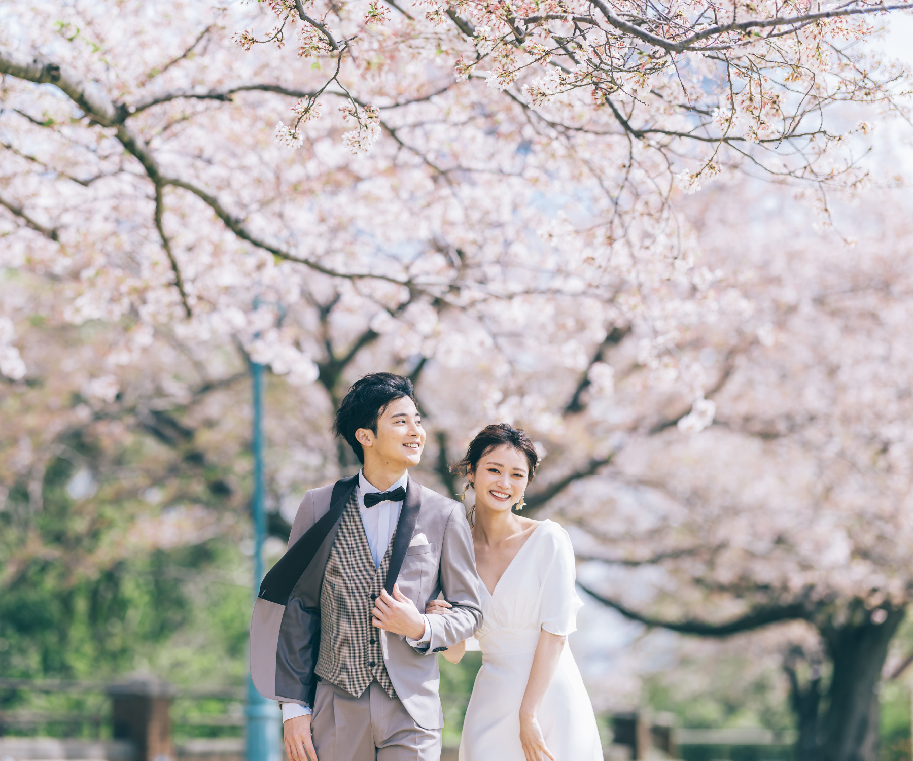 満開の桜の下を笑顔で歩く新郎新婦様のウェディングフォト