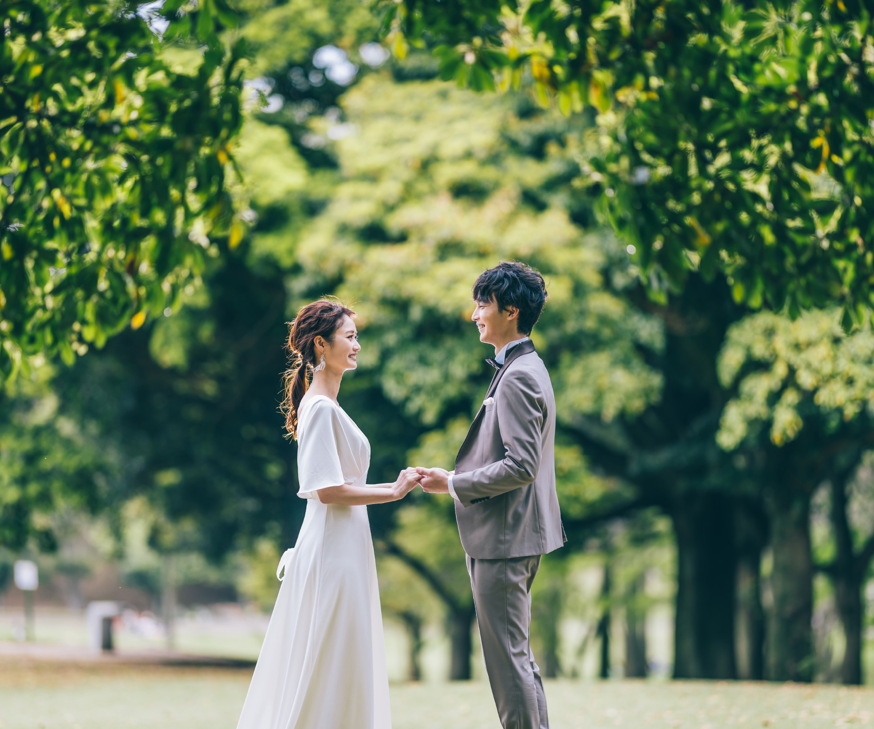 新緑の中で手を繋いで見つめ合う新郎新婦様のウェディングフォト