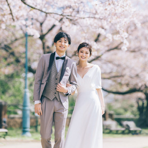 咲き乱れる桜の中腕を組む新郎新婦様のウェディングフォト