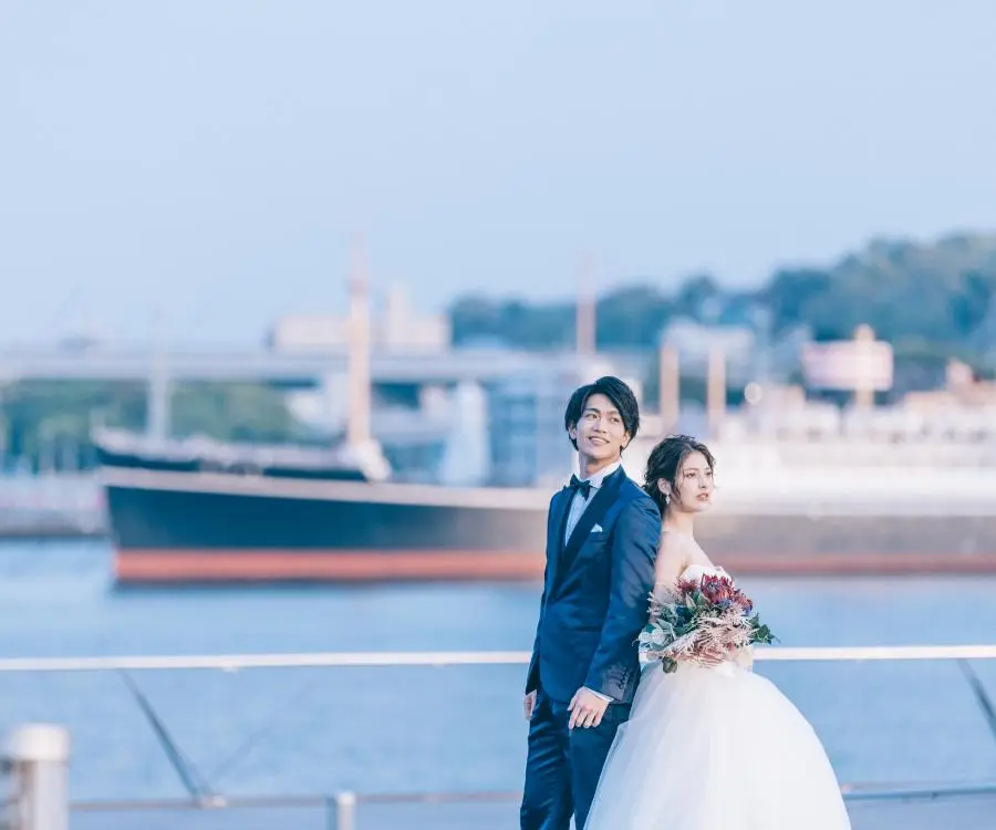 フェリーと海を背景に背中を預けあう新郎新婦様のウェディングフォト