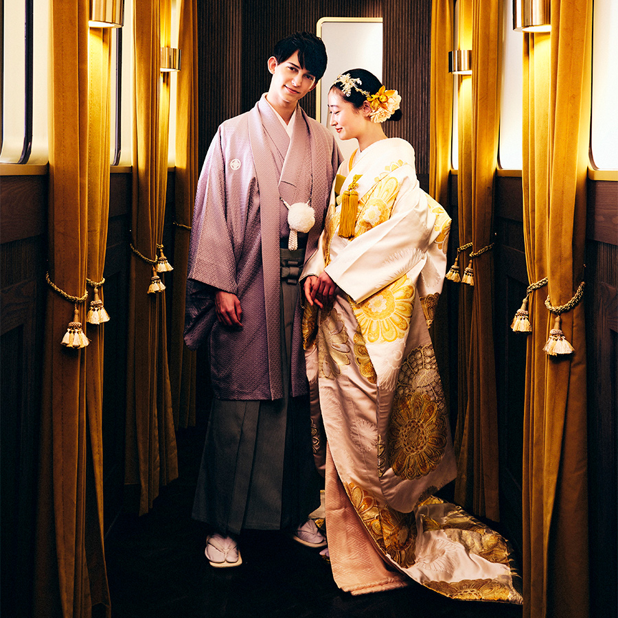      ラグジュアリーなゴールドのカーテンの間でポーズをとる新郎新婦様の結婚写真               