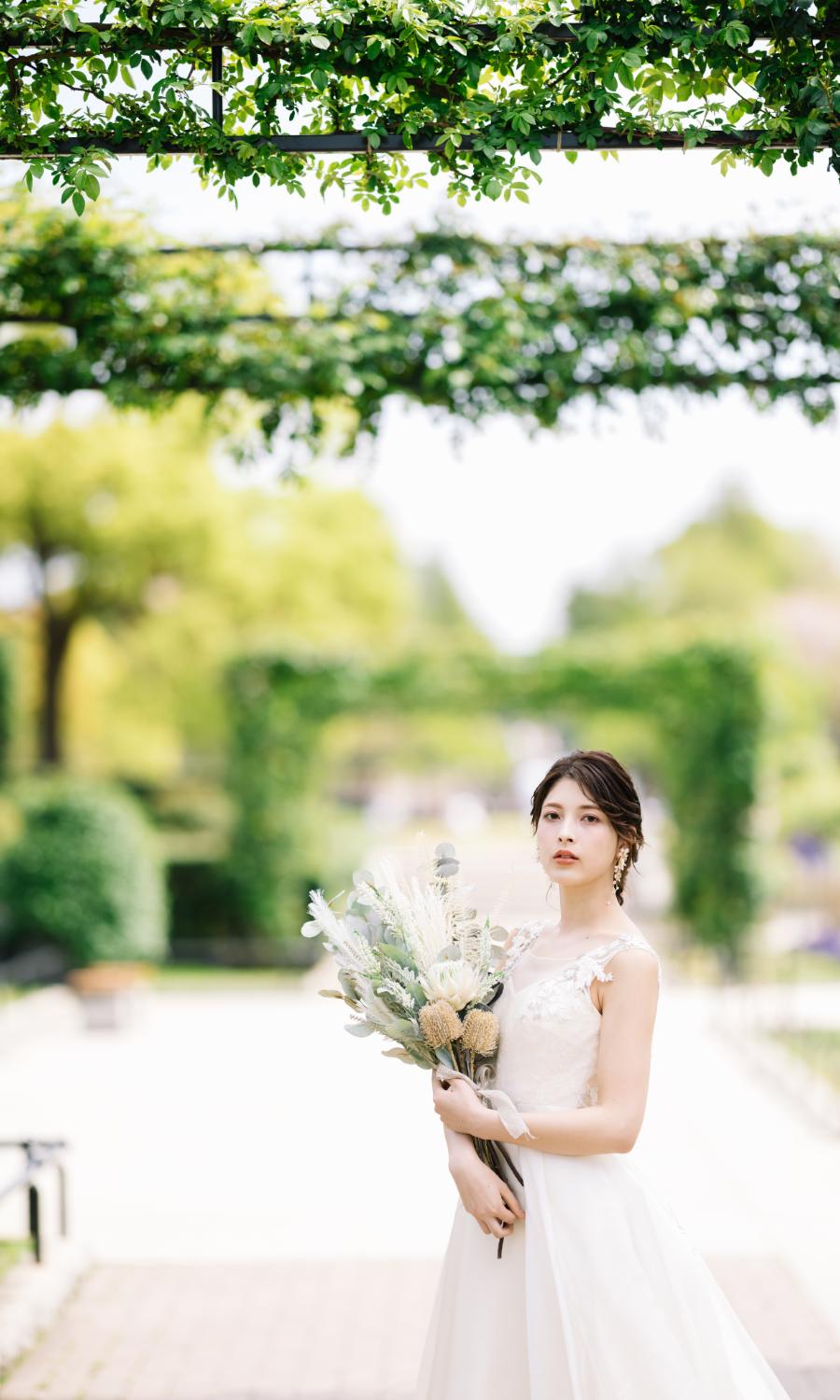 バラ園で花束をもって凛とした表情をする新婦様のウェディングフォト